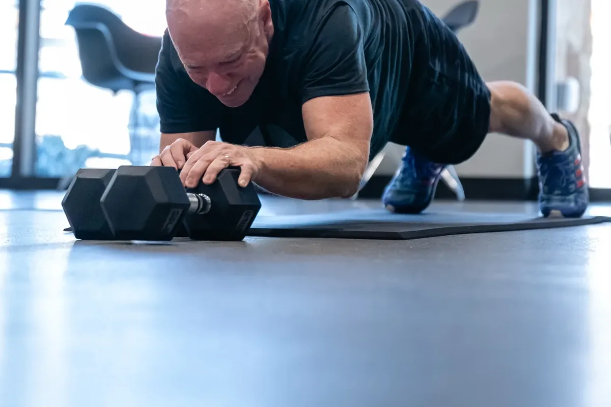 A member braces through a plank while gripping a dumbbell on the training floor at Alloy Personal Training Middleton in Middleton, WI.