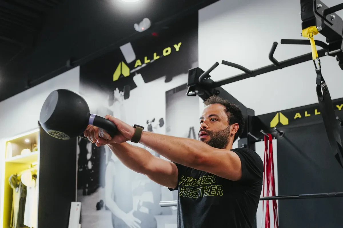 A member swings a kettlebell to eye level, training the hip power behind a pickleball serve, at Alloy Personal Training Middleton in Middleton, WI.