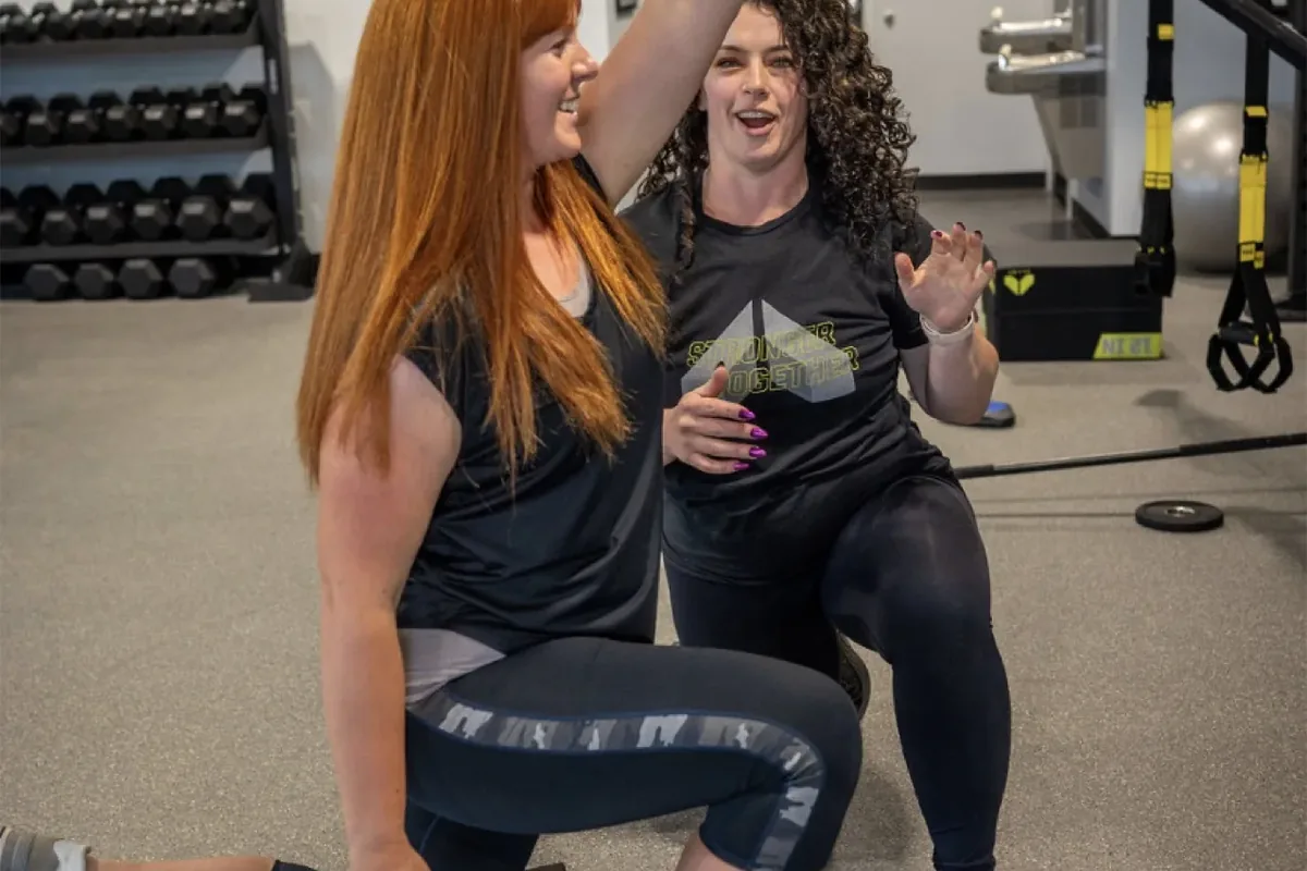 A coach guides a member through a kneeling overhead barbell press at Alloy Personal Training Middleton in Middleton, WI.