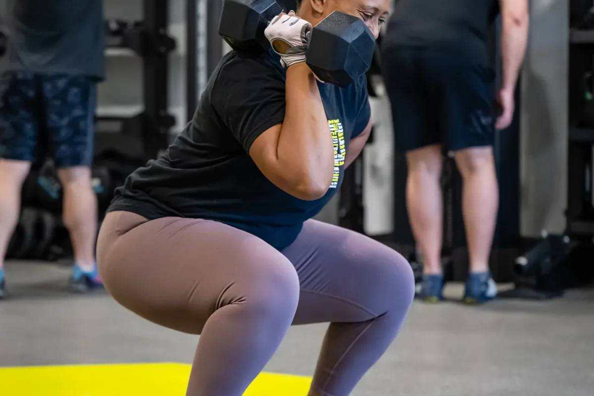 A member performs a dumbbell front squat while two others train at the rack behind her at Alloy Personal Training Middleton in Middleton, WI.